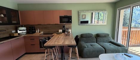 A modern kitchen with a dining area, a sofa set, and a table with a glass cover.