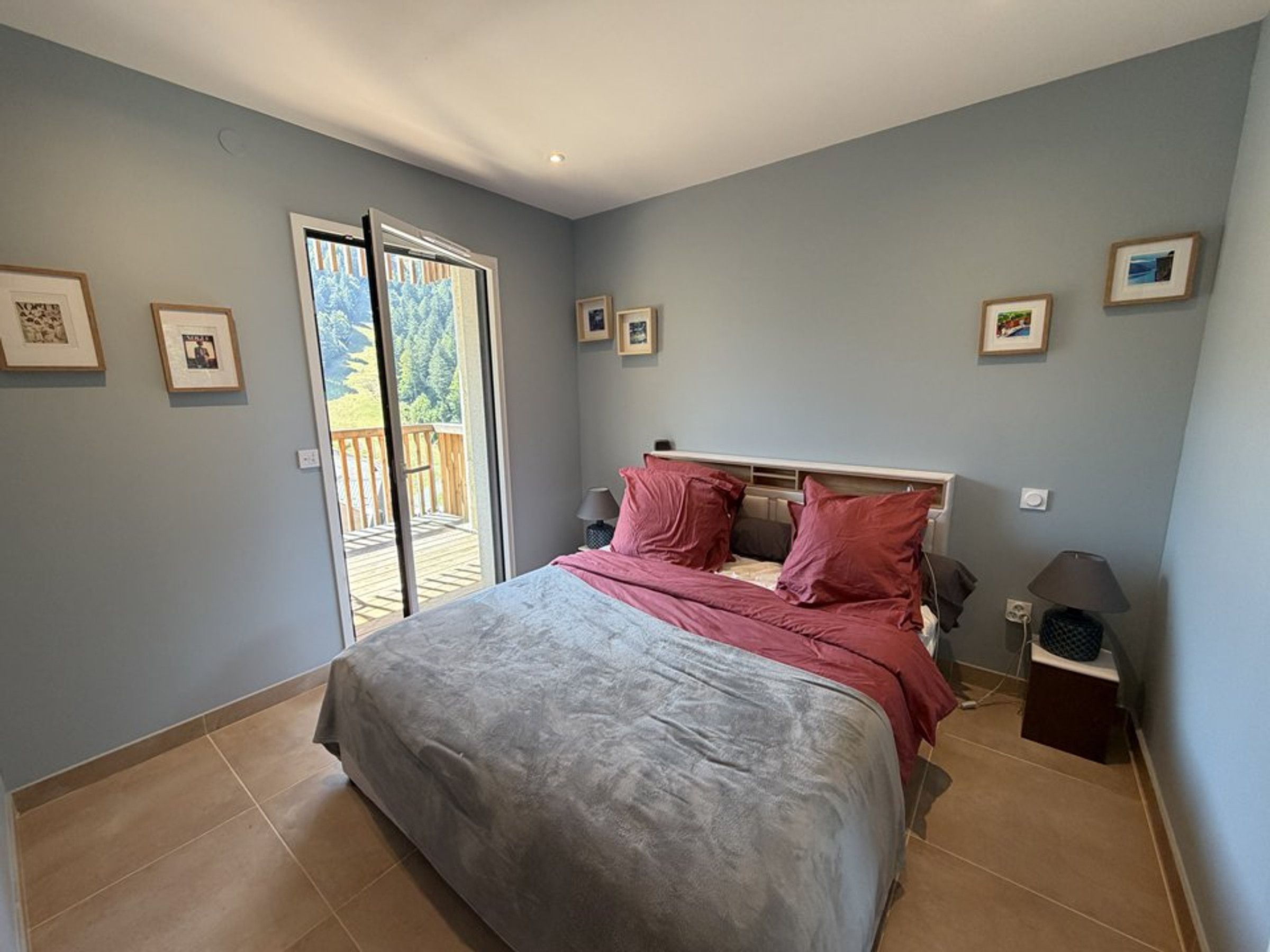 Une chambre à coucher comprenant un lit, une table de chevet, une lampe et une porte-fenêtre coulissante donnant sur une terrasse extérieure.