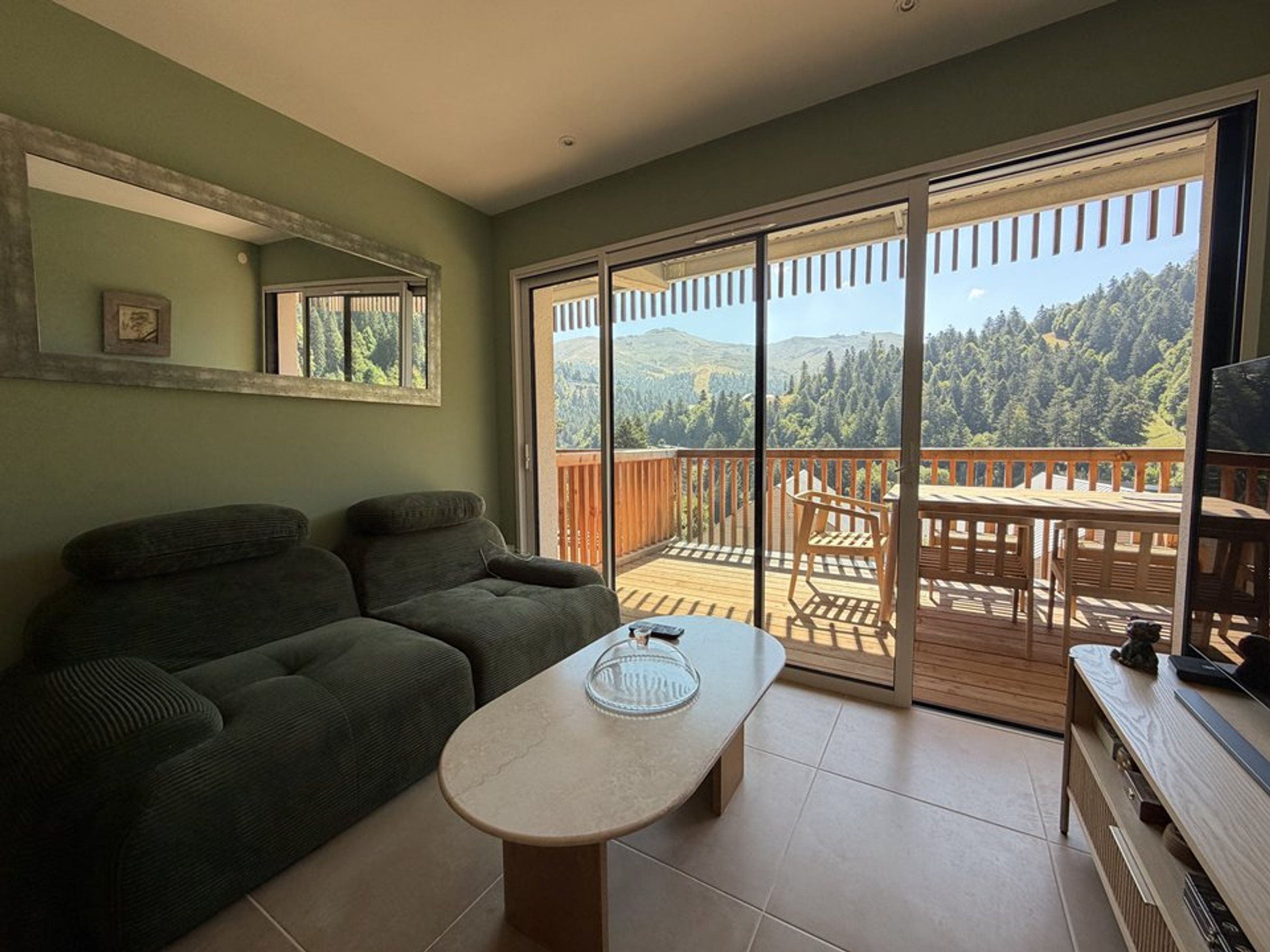 A living room with a sofa, a coffee table, and a balcony with a view of a forested landscape.