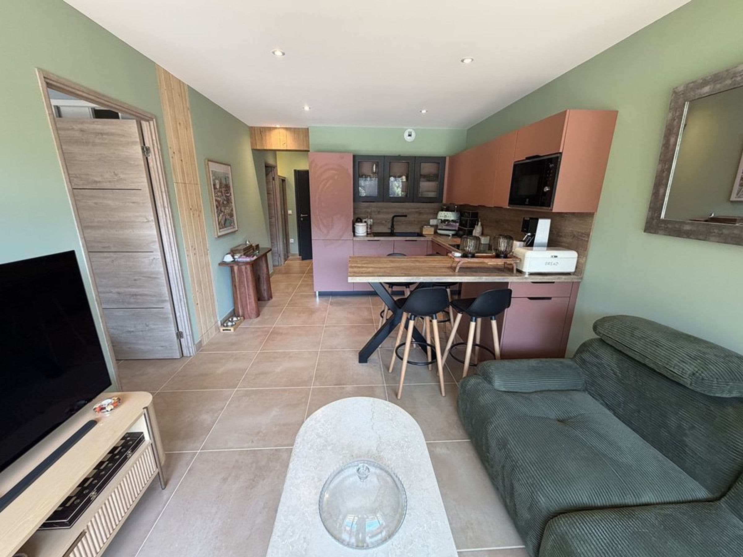 Un salon moderne avec un téléviseur à écran plat, une table basse en pierre et un canapé vert.
