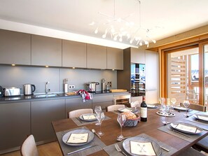 A modern kitchen with built-in appliances and a dining area set for a meal. - Spacious apartment, slopes view - 8 guests (Huez)