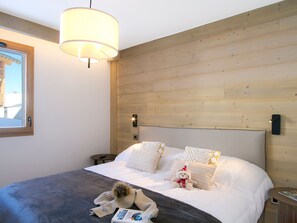 A bedroom with a large bed, wooden headboard, and a hanging light fixture. - Spacious apartment, slopes view - 8 guests (Huez)