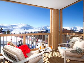 A balcony with a view of snow-covered mountains, wooden furniture, and a table with a glass of orange juice. - Spacious apartment, slopes view - 8 guests (Huez)
