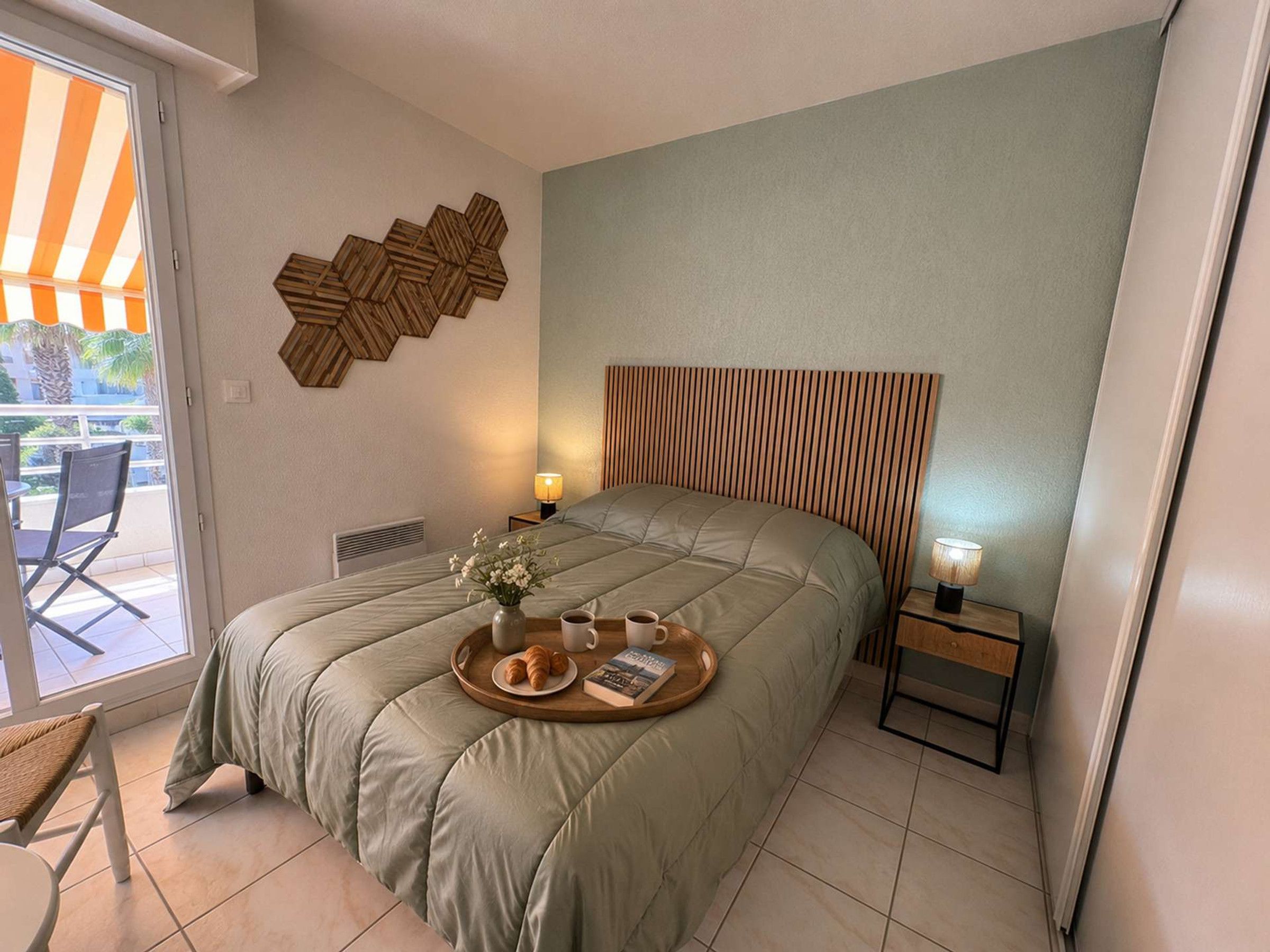 A bedroom with a bed, a bedside table, a tray with a book and a cup, and a wall decoration.