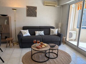 Ein modernes Wohnzimmer mit einem grauen Sofa, zwei Beistelltischen und einem Couchtisch. Darüber hängt eine Wanddekoration und an der Wand befindet sich eine Klimaanlage.