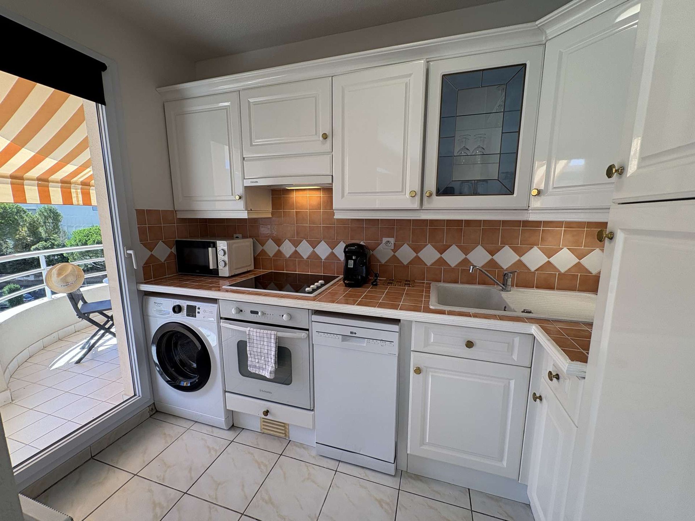 A compact kitchen with white cabinets, a microwave, a toaster, a coffee maker, a sink, and a washing machine.