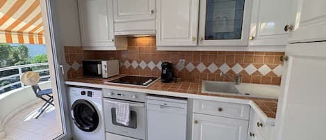 A compact kitchen with white cabinets, a microwave, a toaster, a coffee maker, a sink, and a washing machine.