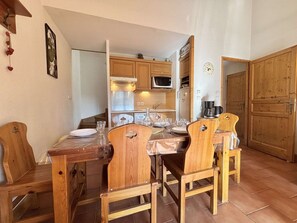 A dining area with wooden chairs and a table, a kitchen with wooden cabinets and appliances, and a clock on the wall. - Apartment with mountain view - 6 guests (Praz-sur-Arly)