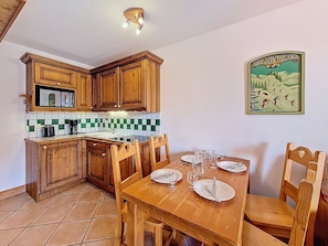 A kitchen with wooden cabinets, a tiled backsplash, and a dining table set for four. - Spacious apartment, balcony - 4 guests (Les Menuires)
