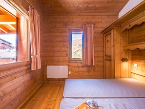 A wooden cabin room with a bed, a window with curtains, and a radiator. - Spacious 2-room apartment with terrace - 4 people (Les Menuires)