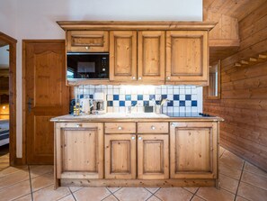 Eine Küche mit Holzausstattung, einer Mikrowelle, einer Kaffeemaschine und einer gefliesten Spritzschutzwand.