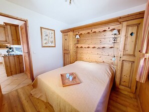Ein Zimmer mit Holzboden, einem Bett, einem kleinen Tisch mit Tassen und einer Tür zu einer Küche.