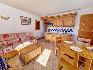 A cozy living room with a sofa and a wooden dining table set for four. - Spacious apartment near slopes - 4 guests (Les Menuires)