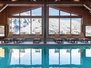 Ein Poolbereich mit Liegestühlen und großen Fenstern, die Blick auf schneebedeckte Berge bieten.
