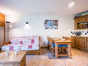 A cozy living room with a sofa, a dining table with chairs, and a kitchen area with wooden cabinets. - Spacious apartment near slopes - 4 guests (Les Menuires)
