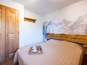 A bedroom with a wooden door, a bed with a wooden headboard, a mountain mural on the wall, and a tray with cups and a pot on the bed. - Spacious apartment near slopes - 4 guests (Les Menuires)