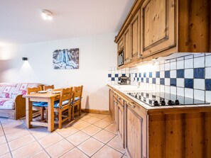 A kitchen with wooden cabinets, a tiled backsplash, and a dining area with a table and chairs. - Spacious apartment near slopes - 4 guests (Les Menuires)
