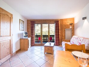 Een kamer met houten vloer, een eettafel met stoelen, een bank, een kitchenette en een balkon met uitzicht op de omgeving.