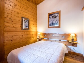 A wooden-paneled room with a bed, two bedside lamps, and two framed pictures on the wall. - Spacious apartment with pool - 6 guests (Les Menuires)