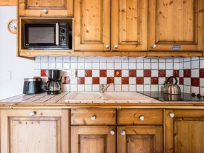 A kitchen with wooden cabinets, a microwave, a kettle, a coffee maker, and a tiled backsplash. - Spacious apartment with pool - 6 guests (Les Menuires)