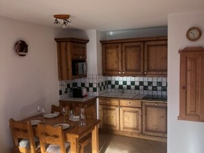 Eine Küche mit Holzschränken, einer gefliesten Spritzschutzwand und einem Esstisch für vier Personen.