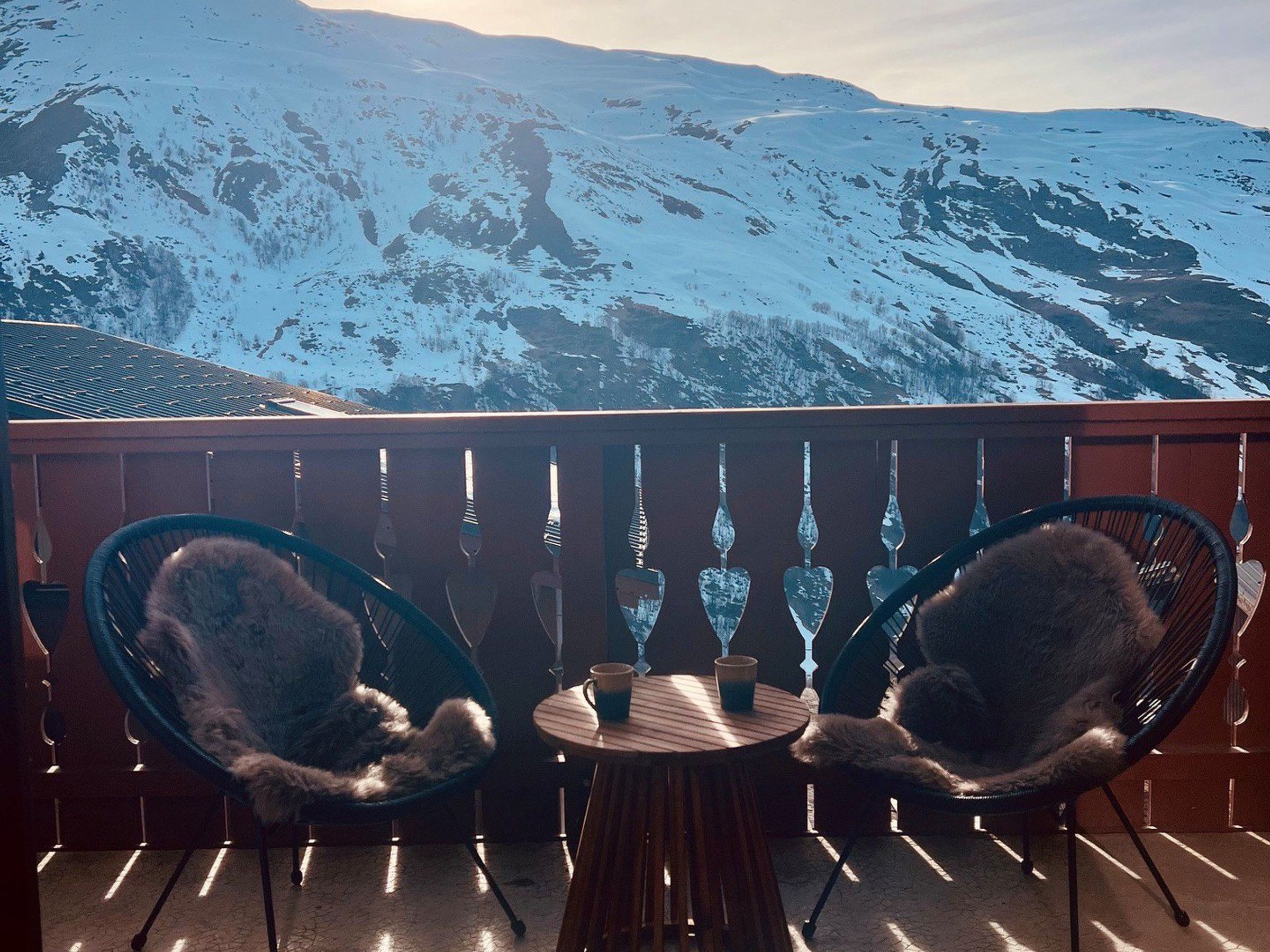 Un balcon avec deux chaises et une table, donnant sur une chaîne de montagnes enneigées.