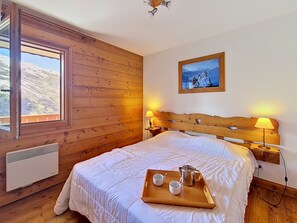 Een slaapkamer met een houten hoofdeinde, een bed met witte lakens, een raam met uitzicht op een berg en een schilderij aan de muur.