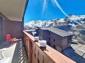 A balcony with a view of snow-covered mountains, a red chair, and a table with a white mug and cup. - Apartment near slopes with balcony (Les Menuires)