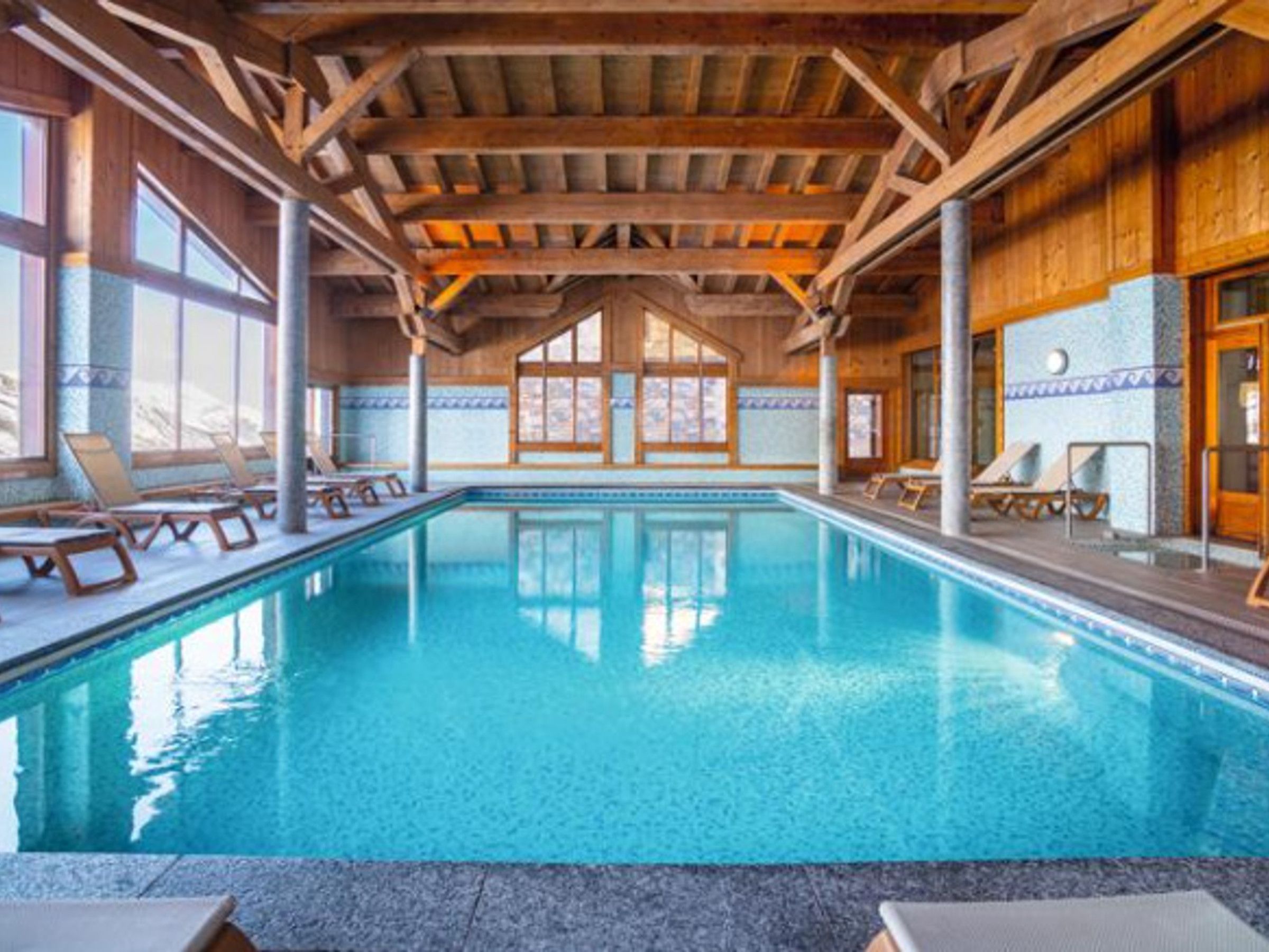 Une piscine intérieure avec des poutres en bois, des murs carrelés et des chaises longues.