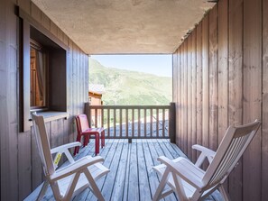 A wooden deck with two white chairs and a red chair, overlooking a mountainous landscape. - Cozy apartment near slopes - 4 guests (Les Menuires)