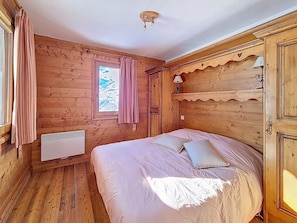 Ein Zimmer mit Holzboden, einem Bett, einem Fenster mit Vorhängen, einem Wandheizkörper und einer Deckenleuchte.