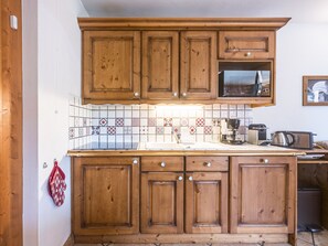 A kitchen with wooden cabinets, a microwave, and a tiled backsplash. - Spacious apartment near slopes - 6 guests (Les Menuires)