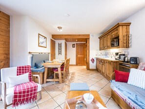 A cozy living room with a sofa, a dining table, and a kitchen area with wooden cabinets and a tiled backsplash. - Spacious apartment near slopes - 6 guests (Les Menuires)