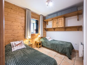 A room with two beds, a wooden wall, a window with curtains, a desk, and a shelf with cabinets. - Spacious apartment near slopes - 6 guests (Les Menuires)