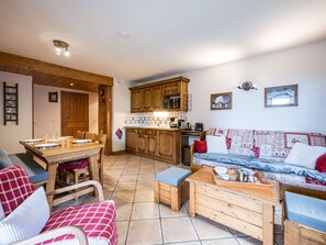 A cozy living room with a wooden sofa, a dining table set for four, and a kitchen area with wooden cabinets and a tiled backsplash. - Spacious apartment near slopes - 6 guests (Les Menuires)