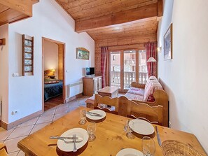 Un interior de madera con una mesa de comedor para cuatro personas, una cama, un televisor y vistas al exterior.