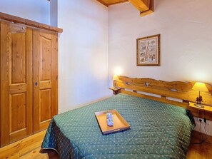 A bedroom with a wooden wardrobe, a bed with a green quilt, a bedside table with a lamp, and a framed picture on the wall. - Bright apartment near slopes - 4 guests (Les Menuires)