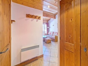 A hallway with a wooden door, a radiator, and a patterned sofa in the background. - Bright apartment near slopes - 4 guests (Les Menuires)