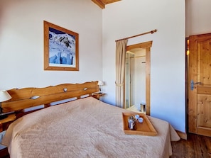 A bedroom with a wooden bed, a bedside table, a framed picture on the wall, a shower area, and a wooden door. - Spacious apartment near the slopes (Les Menuires)