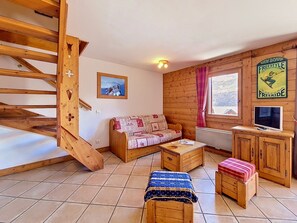 Ein gemütliches Zimmer mit einer Holztreppe, einer Couch, einem Couchtisch und einem Fernseher.