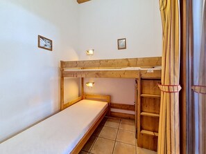 Ein Schlafraum mit Etagenbetten, einem Holzkopfteil, einer kleinen Ablagefläche und einer Wandleuchte.