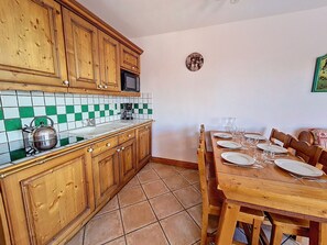 Cuina amb armaris de fusta, resclosa de rajola, un rentapeus i taula de dinar preparada per a quatre amb plats i gots.