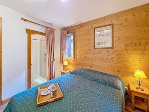 Ein Zimmer mit einem Bett, einer Holzwand, einem Fenster mit Vorhängen, einer Tür und einem kleinen Tisch mit Tablett.