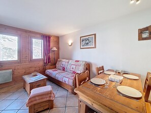 Ein gemütliches Zimmer mit Holzboden, einem Bett mit gemusterten Textilien, einem kleinen Tisch mit Lampe und einem Esstisch für zwei Personen.