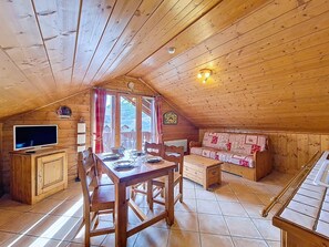 Ein gemütliches Holzhaus mit Essbereich, einer Couch und einem Fernseher.