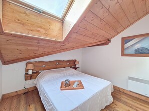 Ein Schlafzimmer mit Holzboden, einem Bett mit weißer Bettdecke, einem Nachttisch mit Lampen und einem Gemälde an der Wand.