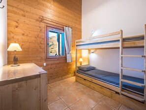 A wooden bunk bed room with a window, a desk with a lamp, and a view of the outdoors. - Spacious apartment near the slopes (Les Menuires)
