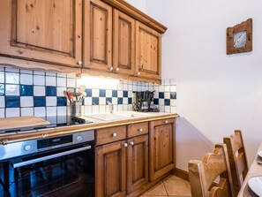 A kitchen with wooden cabinets, a Bosch oven, a coffee maker, and a tiled backsplash. - Spacious apartment near the slopes (Les Menuires)