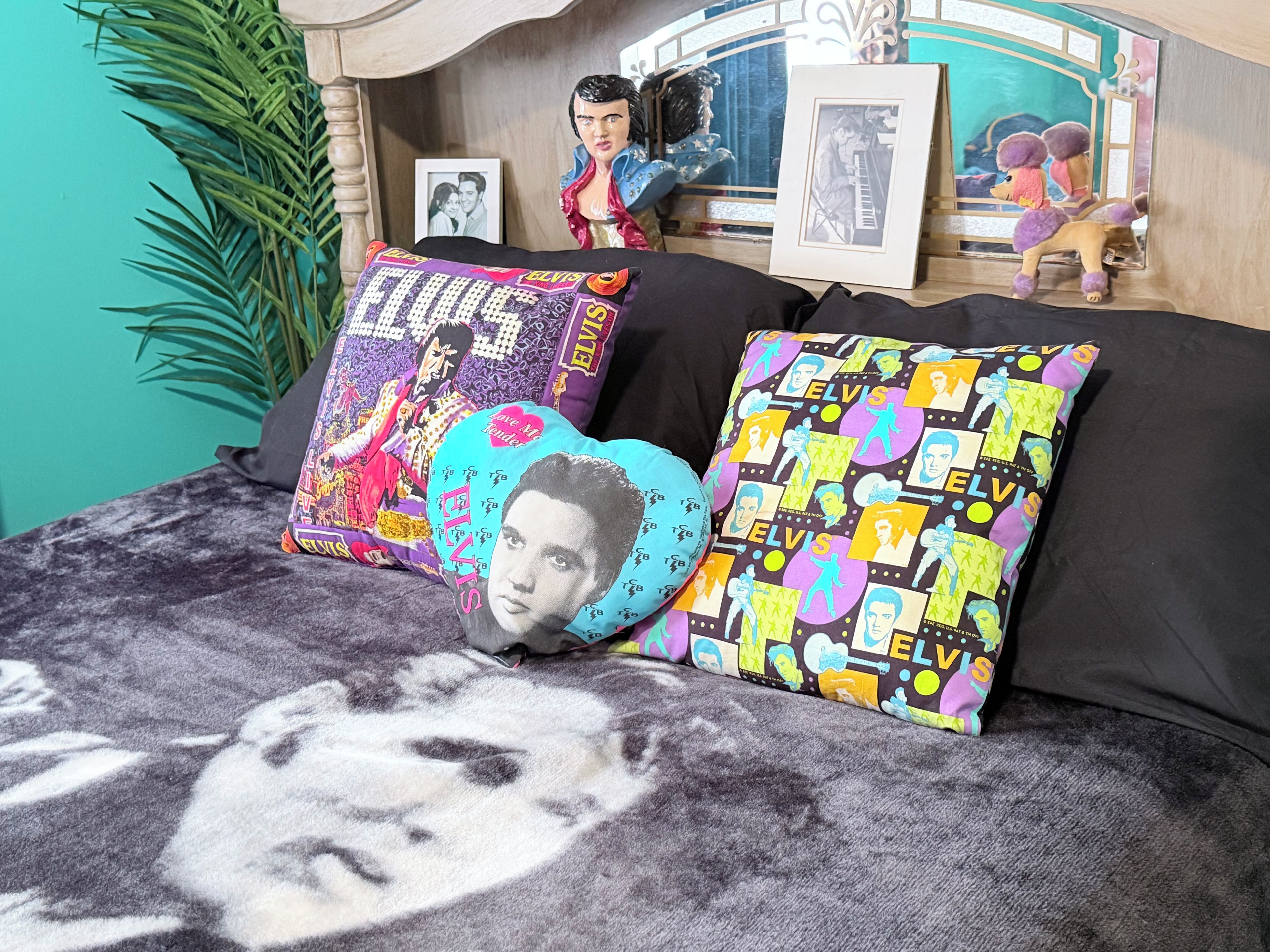 Een bed met zwarte beddengoed, twee kussens met afbeeldingen van Elvis Presley, een ingelijst portret van Elvis, en een kleine beeldjes.
