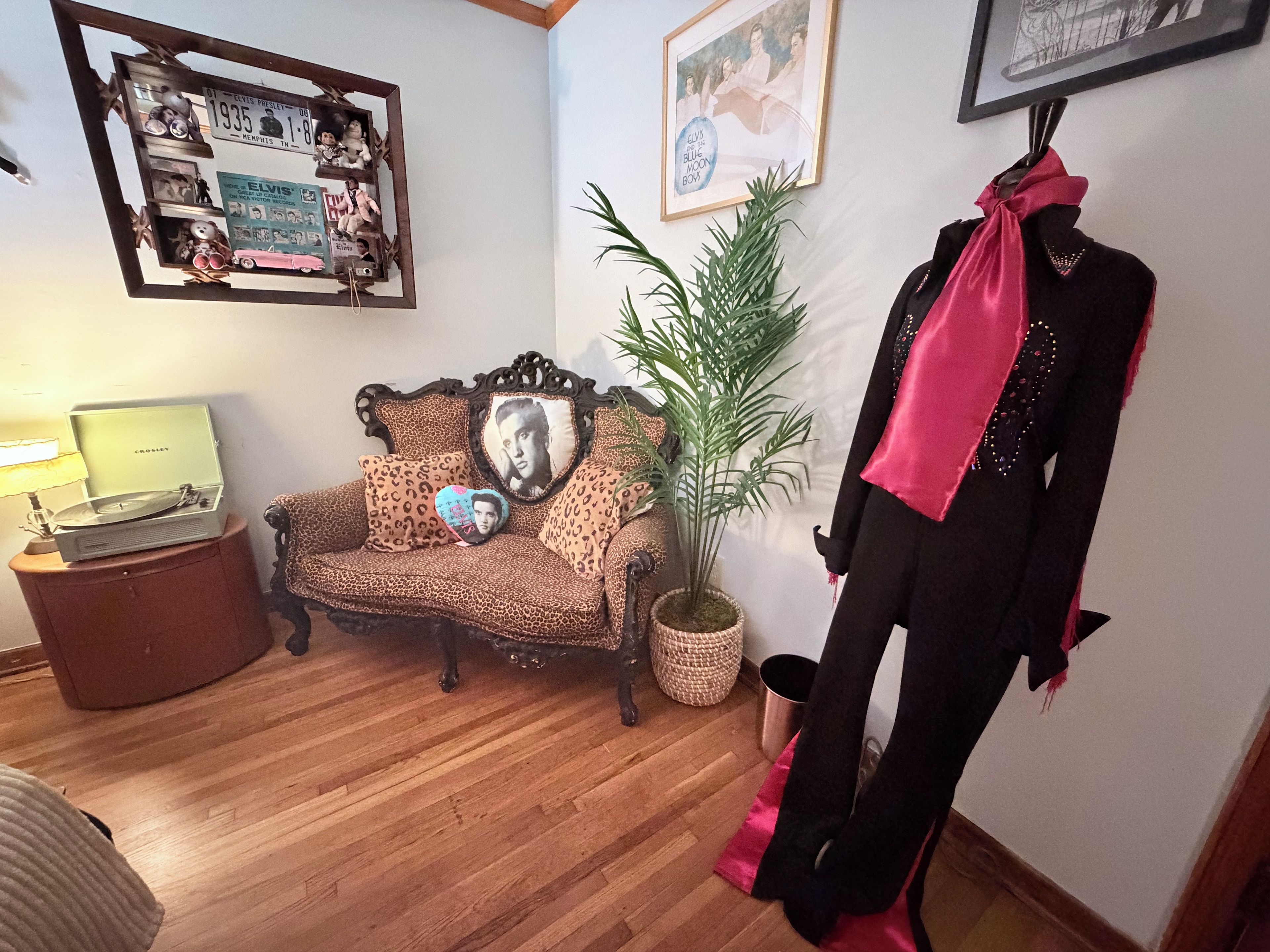 Een kamer met een vintage bank, een plant, een etalagepop en een wand met ingekaderde foto's.